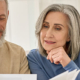 Middle aged couple reading paper bills calculating pension using laptop at home.