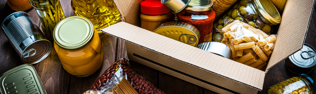 Items of food in a box and on a table, including pasta, vegetable oil, canned peaches