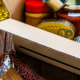 Items of food in a box and on a table, including pasta, vegetable oil, canned peaches