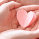 Older person's hands holding a child's hands, which are holding a pink paper heart