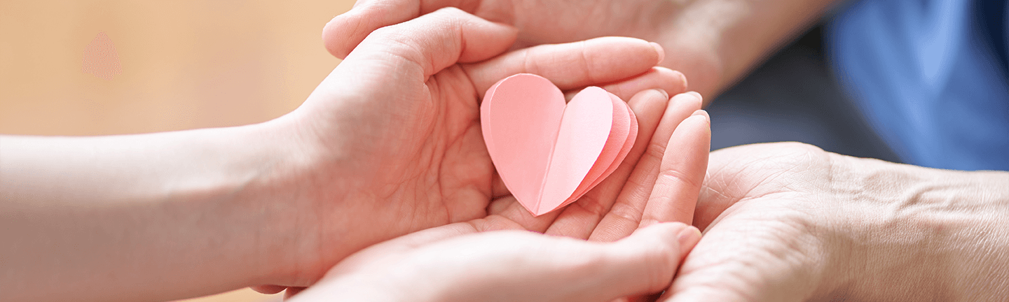 Older person's hands holding a child's hands, which are holding a pink paper heart