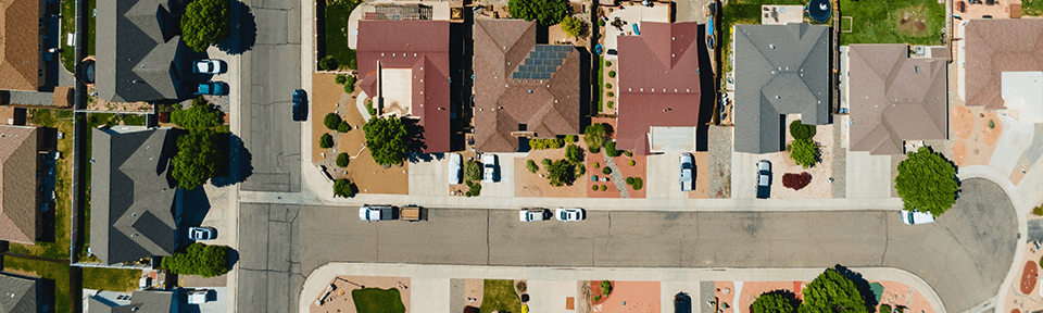 Overhead view of a neighborhood of houses facing a residential street with cars parked on it