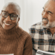 An older couple sit holding a sheaf of paper, facing another person whose face we cannot see